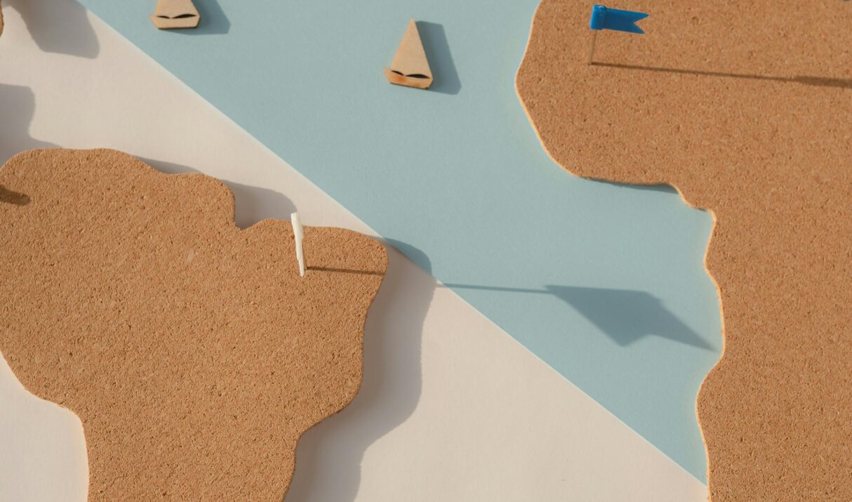 Cork cutout world map on pastel background with blue flags, ideal for geography and travel planning.